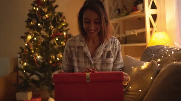 Πορτρέτο περιχαρής αστεία γυναίκα άνοιγμα χριστουγεννιάτικο κουτί δώρου για Χριστούγεννα εορτασμού του χρόνου στο σπίτι. Έκπληκτη κοπέλα φορώντας χαριτωμένο πυτζάμα ψάχνει για δώρο κουτί — Αρχείο Βίντεο
