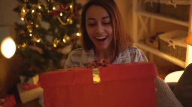 POV mutlu ve çok mutlu bir bayanın Noel hediyesini evde Noel zamanı kutlaması olarak görüyor. Sevimli pijama giyen, duygusal olarak hediye kutusuna bakan sürpriz bir kız.