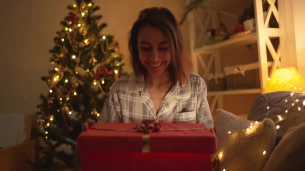 Pomalý film šťastný nadšený hezká žena otevření vánoční dárkové krabice na x-mas čas oslavy doma. Překvapená dívka na sobě roztomilé pyžama hledá dárkové krabice se světlem uvnitř — Stock video