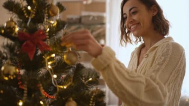 Güzel gülümseyen kadının yavaş çekimleri evdeki yılbaşı ağacını ampullerle süslüyor. Evin içinde güzel bir atmosfer yapıp Noel 'i ve yeni yılı kutluyoruz.