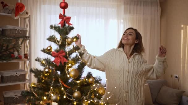 4k slow motion of happy pretty woman dancing with Christmas lights at cozy festive home with christmas tree. xmas and happy new year at home athmosphere concept — Stock Video