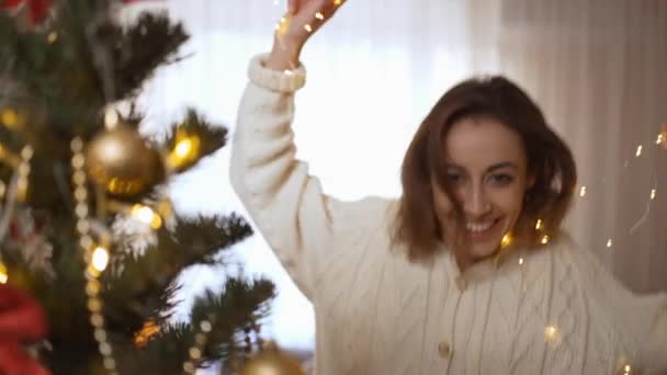 Navidad y feliz año nuevo en casa athmosphere concepto. 4k cámara lenta de cerca alegre riendo elegante mujer bailando con luces en casa acogedora con árbol de Navidad — Vídeos de Stock