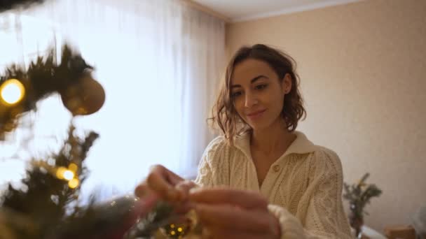Närbild slow motion av elegant kvinna hänger upp gyllene boll på festlig julgran. om att göra trevlig mysig atmosfär i heminredning och fira jul och gott nytt år — Stockvideo