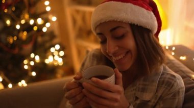 Pijamalı ve kırmızı Noel Baba şapkalı bir kadın kanepeye oturmuş televizyon izliyor ve kupasından sıcak çikolata içiyor. Noel arifesinde, Noel arifesinde dinleniyor. Rahat bir evde ışıklar ve yılbaşı ağacıyla süslenmiş bir kız.