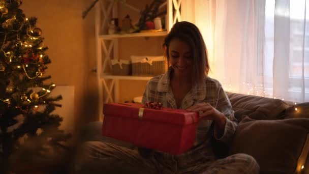 Câmera lenta feliz alegrou mulher bonita abrindo caixa de presente de Natal em x-mas celebração do tempo em casa. Menina surpresa vestindo pijama bonito olhando para caixa de presente com luz para dentro — Vídeo de Stock