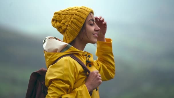 Rallentatore Vista laterale b-roll donna turistica in giallo usura in piedi sul prato con bella vista sulle montagne. Ragazza zaino in spalla in avanti e prepararsi a escursioni — Video Stock