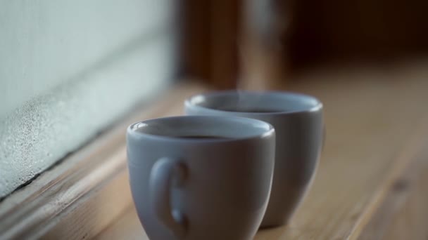 Close up side view Két csésze forró ital kávé ablak mellett, víz páralecsapódás ablak üveg, kora reggel, ébredés koncepció — Stock videók