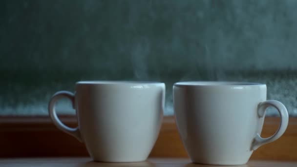 Dos taza de café de bebida caliente cerca de la ventana, condensación de agua en el vidrio de la ventana, temprano en la mañana, despertar concepto — Vídeos de Stock