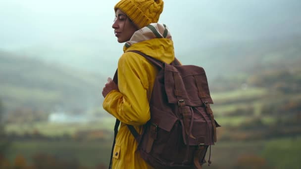 Slow motion Vue de côté b-roll touriste femme en jaune usure debout sur prairie avec belle vue sur les montagnes. Backpacking fille impatiente et se préparer à la randonnée — Video