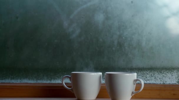 Pencerenin yanında iki fincan sıcak kahve, cam camında su buharlaşması, sabahın erken saatlerinde uyanma kavramı. — Stok video