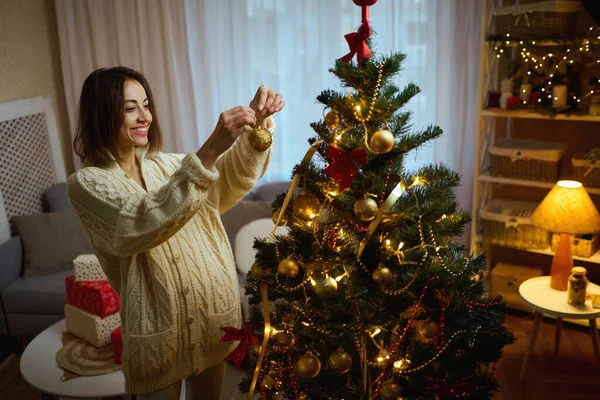Kaunis nainen viihtyisässä talvipuserossa koristelu joulukuusi kotona, valmistautuu uudenvuoden aikaan — kuvapankkivalokuva