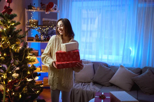 ผู้หญิงมีความสุขถือกล่องของขวัญคริสต์มาสโดยการตกแต่งต้นคริสต์มาสที่บ้านเทศกาลภายใน — ภาพถ่ายสต็อก
