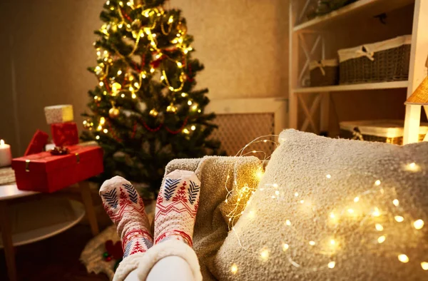 Piernas de mujer en calcetines de Navidad en el interior de la casa decorada con árbol de Navidad en el fondo — Foto de Stock