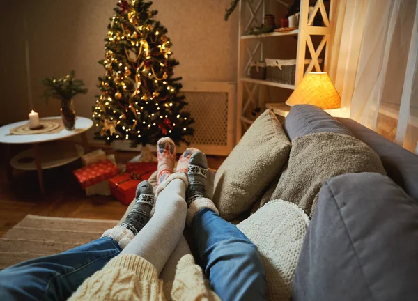 Talvilomat. Pari lepää kotona koristeltu valot ja joulukuusi, valokuva jalat villasukat — kuvapankkivalokuva