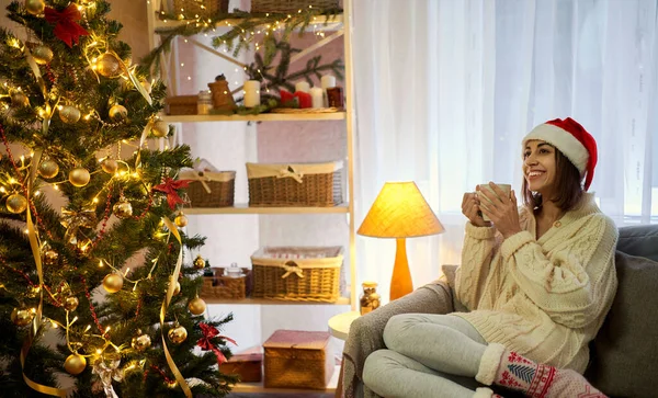 Nainen punaisessa jouluhatussa juo kuumaa kaakaota, rentouttaa jouluaattona, uusi vuosi — kuvapankkivalokuva