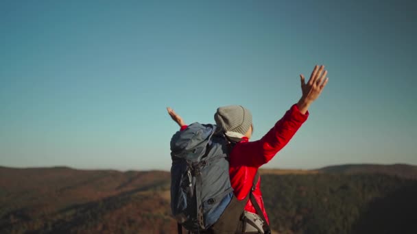 Zadní pohled zpomalit b-roll Svoboda žena pěší turistka s batohem zvedající ruce těší krásné krajiny v horách, stojí proti modré obloze při západu slunce — Stock video