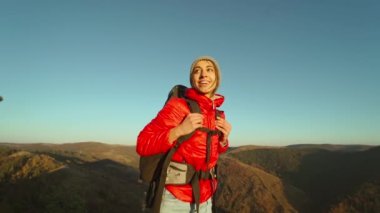 Kırmızı ceketli ve bereli gülümseyen genç bir kadının portresi gün batımında dağın tepesinde yürüyüş yaparken kendinden emin ve mutlu görünüyordu.