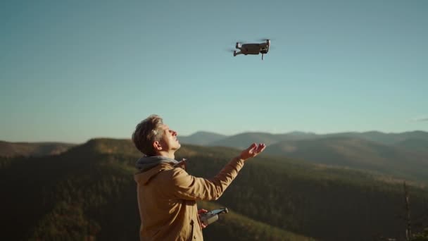 Hombre piloto con mando a distancia al aire libre en la naturaleza salvaje. Fotógrafo aéreo profesional y operador de drones aterrizando dron en su mano después del vuelo y la filmación. Bosque de pinos y paisaje de montaña — Vídeo de stock