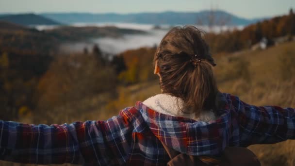 Kareli ceketli mutlu kadın yürüyüşçü dağın tepesinde duruyor, kollarını havaya kaldırıyor ve sonbahar gündoğumunda dağın tepesindeki bulutların üstünde görünmekten hoşlanıyor.. — Stok video