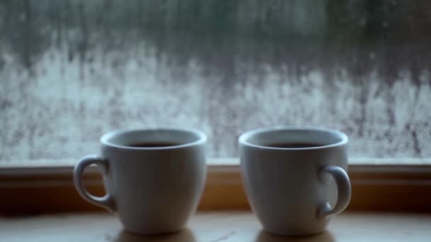 Két csésze forró kávé az ablak mellett, víz páralecsapódás az ablaküvegen, kora reggel, ébredés koncepció — Stock videók