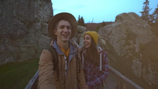 Feliz casal sorridente caminhante caminha juntos no parque nacional Tustan na Ucrânia. homem e mulher fazendo sefie em paisagem incrível com abetos, montanhas rochas e céu pôr do sol no fundo — Vídeo de Stock