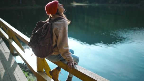 Slow motion geïnspireerde vrolijke vrouw wandelaar zit op houten pier bij prachtige bergmeer met turquoise water en geniet van verbazingwekkende rustige herfst landschap. wilde natuur schoonheid, gezonde actieve levensstijl — Stockvideo