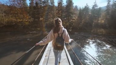 Ağır çekimde Millennial kadınının tek başına yaptığı yolculuğun tadını çıkarırken. Sırt çantalı kadın kaşif bir dağ nehri üzerinde asılmış bir köprüde yürüyor. Sürdürülebilir yaşam tarzı, sorumlu seyahat