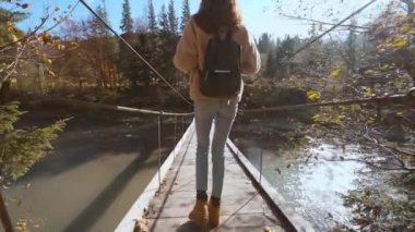 Ağır çekimde Millennial kadınının tek başına yaptığı yolculuğun tadını çıkarırken. Sırt çantalı kadın kaşif bir dağ nehri üzerinde asılmış bir köprüde yürüyor. Sürdürülebilir yaşam tarzı, sorumlu seyahat