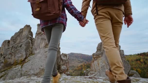 Para trzymających się za ręce spacerujących na świeżym powietrzu w romantycznym widoku na skalisty park narodowy Tustan, Ukraina. Wędrowcy mężczyzna i kobieta miłośnicy trekking chodzenie z plecakami w szlaku w górach — Wideo stockowe