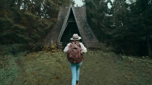 Femme touristique élégante dans un chapeau avec sac à dos à venir dans une vieille cabane en bois de style vintage. Aventure, voyage, exploration — Video