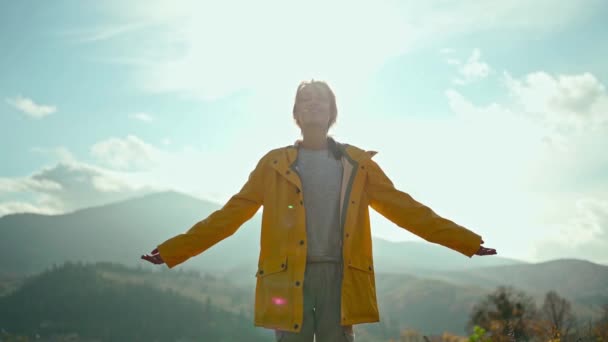 Slow motion retrato cinematográfico bonita Jovem mulher vestindo em casaco amarelo levantando os braços para o céu azul e desfrutando de liberdade e bela vista pacífica acima das nuvens no topo da montanha — Vídeo de Stock