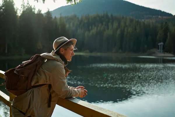 Side View mies reppu ihaillen vuori järvi, nauttia raitista ilmaa metsän — kuvapankkivalokuva