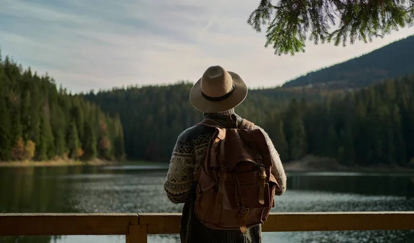 Reisende mann i hatt med ryggsekk stående ved fjellvannet, nyter et fantastisk landskap – stockfoto
