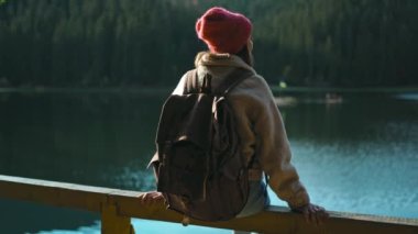 Dikiz manzaralı yürüyüşçü kadın güzel dağ gölü kıyısındaki ahşap iskelede oturur ve muhteşem sakin orman manzarasının tadını çıkarır. Vahşi doğa güzelliği, sağlıklı aktif yaşam tarzı