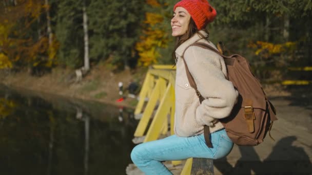 Terug uitzicht geïnspireerde vrolijke vrouw wandelaar zit op houten pier bij prachtige bergmeer met turquoise helder water en geniet van verbazingwekkende rustige herfst landschap. wilde natuur schoonheid, gezonde actieve levensstijl — Stockvideo