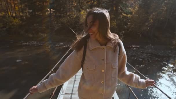 Slow motion portret van gelukkige mooie jonge vrouw toerist staande op houten hangbrug opgehangen over de berg rivier. geweldig landschap met sparren, bergen en lucht op de achtergrond — Stockvideo