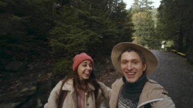 Mutlu çift yürüyüşçüleri yeşil çam arka planında Forest National Park yolunda selfie ya da görüntülü arama yapıyorlar. Hippiler kadın ve şapkalı adam gibi gülümser ve dağ ormanlarında yürür.