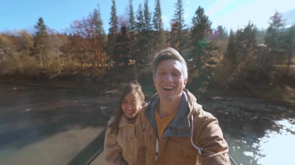 Slow motion happy travelers couple walks together on wooden Suspension Bridge hanged over mountain river. man and woman making sefie on amazing landscape with spruces, mountains and sky on background — Stock Video