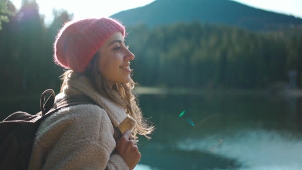 Ağır çekimde ilham veren neşeli kadın yürüyüşçü güzel dağ gölündeki ahşap iskelede turkuaz suyla oturur ve muhteşem sakin sonbahar manzarasının tadını çıkarır. Vahşi doğa güzelliği, sağlıklı aktif yaşam tarzı — Stok video