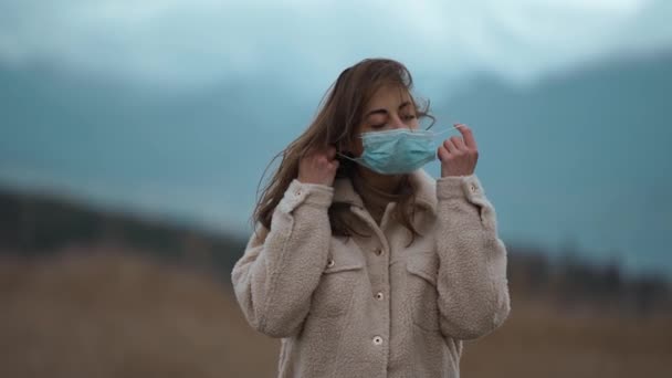 Ağır çekim yorgun kadın koruyucu maskeyi çıkardı dağlarda doğaya el kaldırdı. Salgın konseptinin koronavirüs sonu. Özgür kız elinde koruyucu bir maske tutuyor. covid salgınının sonu — Stok video