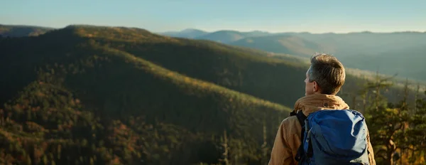 Panoraamanäkymät vuorille ja kukkuloille metsällä auringonlaskun aikaan, mies patikoija ihaillen maisemaa — kuvapankkivalokuva