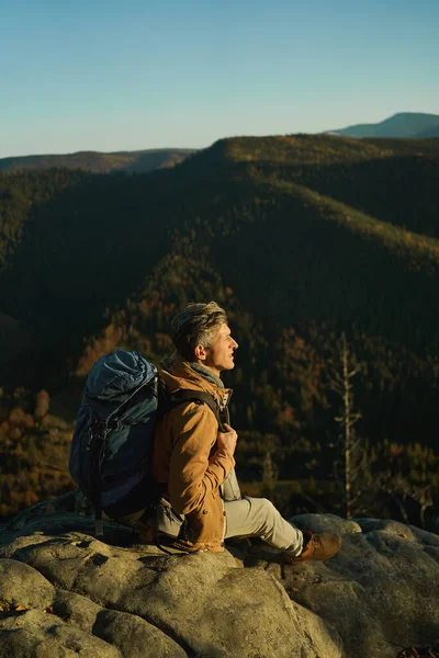 Väsynyt ja innoittamana vaeltaja mies istuu kalliolla ja ihaillen kaunista maisemaa — kuvapankkivalokuva