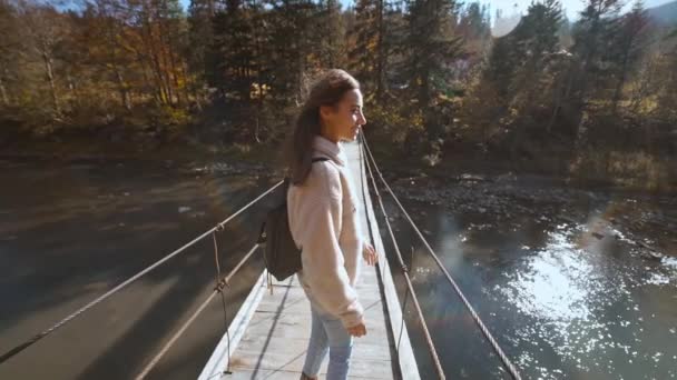 Αργή κίνηση Πίσω όψη της γυναίκας Millennial απολαμβάνοντας ένα σόλο ταξίδι. Γυναίκα εξερευνητής στο καπέλο με σακίδιο περπατά σε μια κρεμαστή γέφυρα πάνω από ένα ποτάμι βουνό. Βιώσιμος τρόπος ζωής, υπεύθυνα ταξίδια — Αρχείο Βίντεο