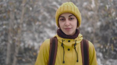Gezgin kadın karla kaplı ormanda yürüyüş yapıyor. Giyinik. Sarı kışlık giysiler ve sırt çantası. Kış geliyor, ilk kar yağışı
