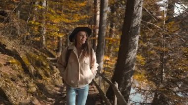 Kadın turist, güneşli bir sonbahar gününde sonbahar ormanında yolda yürüyor. Sırt çantasıyla dağ gölünün etrafındaki ormanda yürüyüş yapan kadın yürüyüşçü. Soğuk güneşli bir sabahta, açık hava macerası.