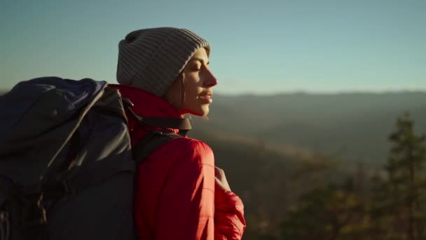 Pomalý film portrét šťastná bezstarostná dívka pěší turistka s batohem relaxační a těší západ slunce pohled na krásnou krajinu v horách, stojí proti modré obloze při západu slunce. selektivní zaměření — Stock video