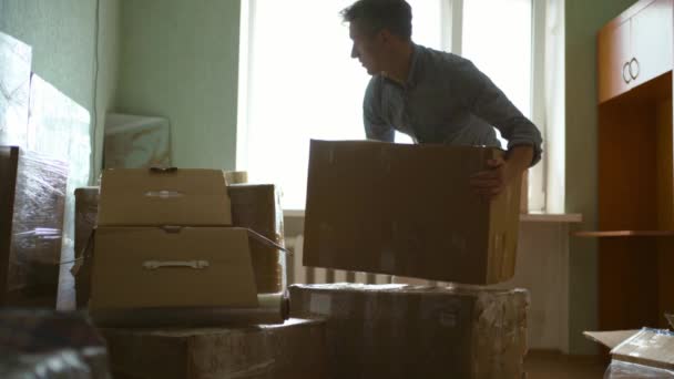 Millennial male renter in living room holding tape dispenser sealing cardboard boxes moving to new house. Leaving tenant apartment, relocation day and packing personal belongings concept — Stock Video