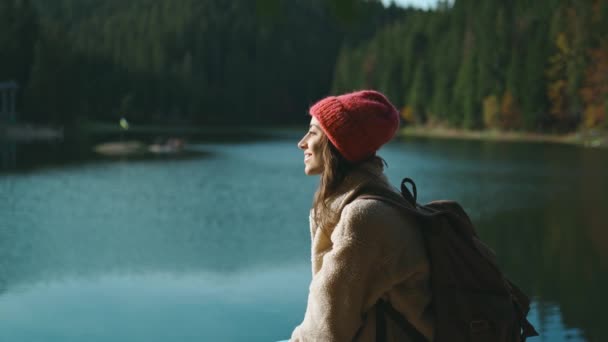 Portrét inspirované krásné usměvavé ženy turistka batohem sedí na dřevěném molu na krásném horském jezeře s tyrkysovou čistou vodou a těší úžasné klidné podzimní krajiny — Stock video