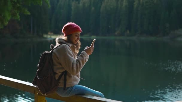 Женщина-хипстер 20-х годов в лесу, делающая селфи на озере Вью. Видеооператор Travel Girl стоит осенью на природе и снимает себя на камеру смартфона, делая видеозвонок — стоковое видео