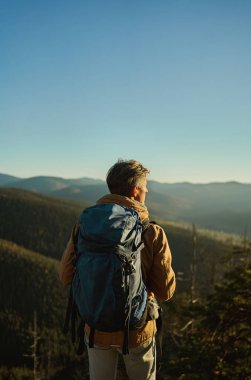 Gün batımında ormanlı dağlar ve tepeler, manzaraya hayran olan insan yürüyüşçüleri.